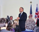 Deval Patrick addressing delegates, with the UK and US flags displayed behind him